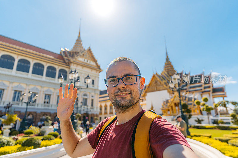 在泰国曼谷大皇宫建筑群的Chakri Maha Prasat王座大厅进行视频通话的年轻人